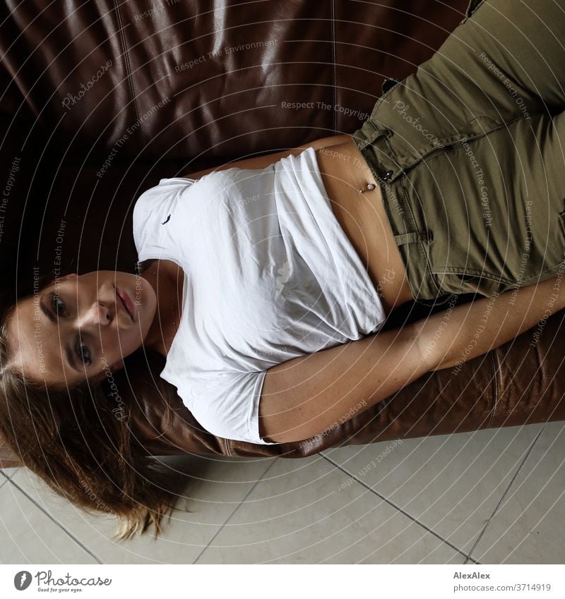 Portrait of a young woman lying on a brown leather couch and looking up into the camera Athletic Feminine empathy Emotions emotionally portrait