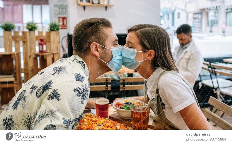 Couple kissing with mask sitting in a restaurant couple coronavirus love closeup covid-19 diner coffee shop romantic date safety protection in love relationship