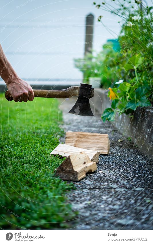 Man chops wood with an axe in the garden. Section. Axe Firewood Chop Garden Grass green out Exterior shot Nature Stack of wood by hand over40 Day Fuel Detail