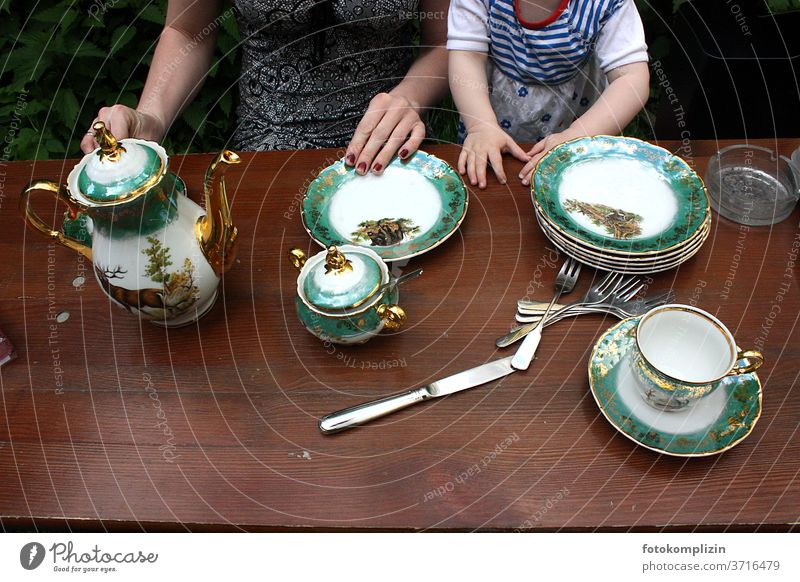 fine green golden porcelain tableware on brown wood table with view on hands of woman and child Porcelain tableware Crockery Plate Cup Pottery can Coffee pot