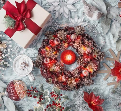 Christmas concept: advent wreath, present, hot chocolate in mug, Christmas flower, snowflakes, Christmas balls, and holly on light blue textile background. Top view