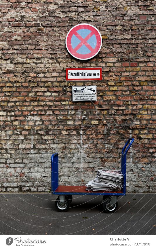 upright in the no stopping area | handcart with newspapers in front of brick wall with no stopping sign Trolley transport trolley piles of newspapers