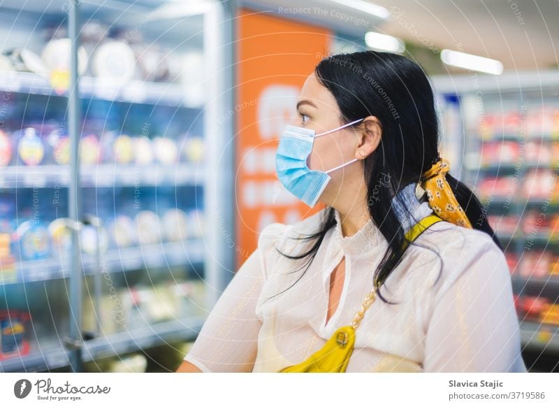 Grocery shopping during COVID-19. Woman wearing a protective face mask and looking at the dairy section of a supermarket while shopping. Selective focus, blank space