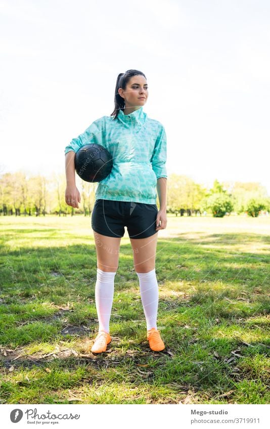 Young female soccer player standing on field holding ball. young football determination preparation female athlete practicing athleticism focused sports