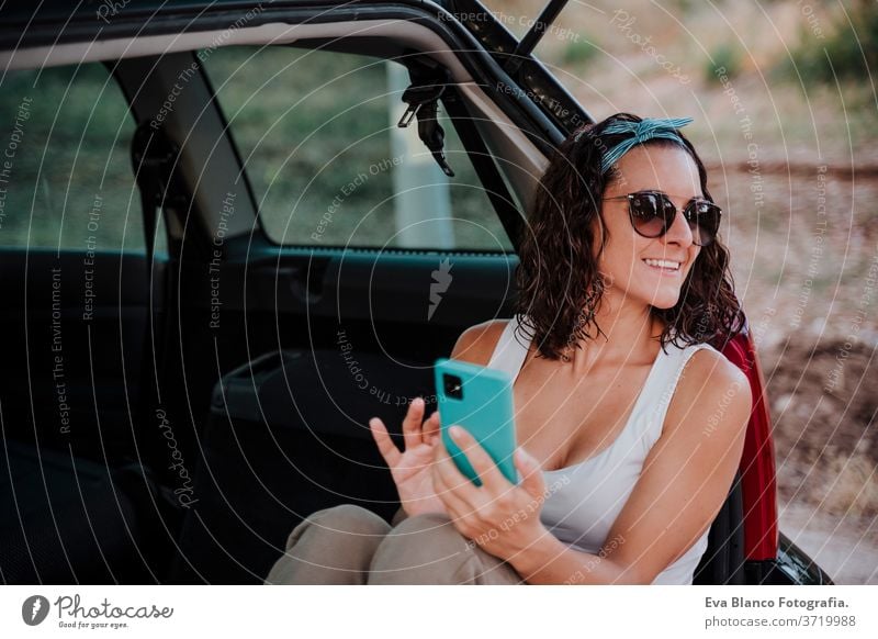 young happy woman in a car using mobile phone. Travel concept travel caucasian smiling outdoors waiting adult contraption communication lifestyle sitting