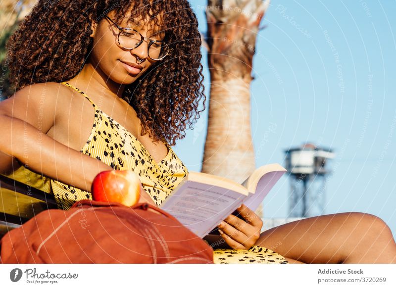 Relaxed ethnic woman reading book in park bookworm relax enjoy interesting story novel female black african american eyeglasses content literature sit bench