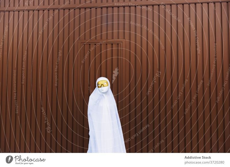 Anonymous child in ghost costume on street halloween mask masquerade kid holiday event autumn city building urban suit scary entertain spooky celebrate season
