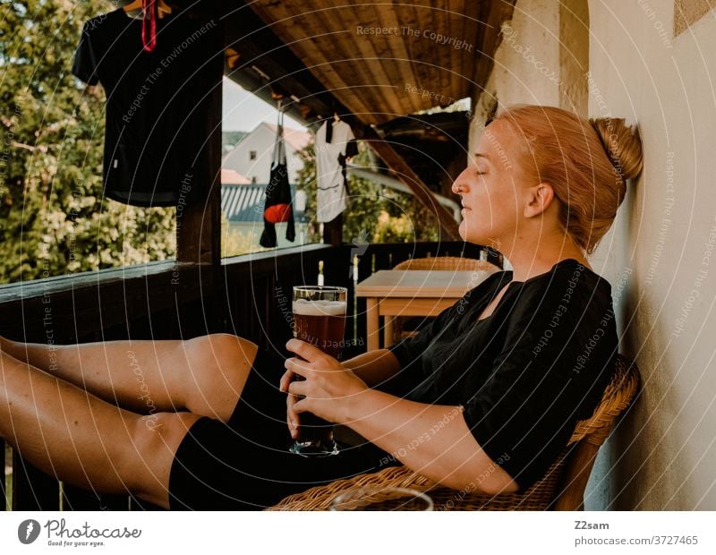 Young woman enjoying a wheat beer on the balcony enjoyment Drinking Beer white beer rest relax Dream Closed eyes Summer Sun Warmth Cycling cycling gear Garden