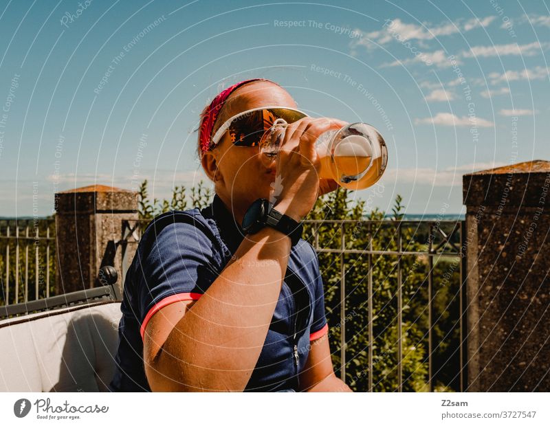 Young woman drinking a wheat beer in the sun Drinking enjoyment white beer Beer Refreshment Sports sportswoman Jersey Cycling Garden Green Nature vacation Trip