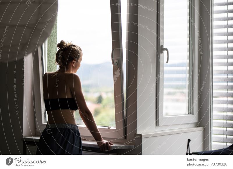Home quarantine and social distancing during covid pandemic. Silhouette of lonley caucasian woman standing by window, anxiously looking out. Coronavirus infection, pandemics, disease outbreaks
