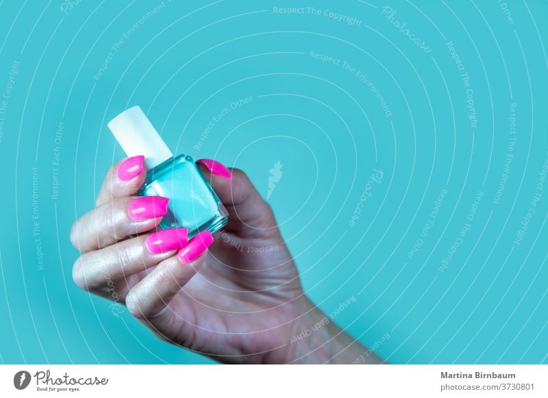 Time to change the color. female manicured hand with pink nail polish holding a bottle of turquoise nail polish shiny fingernail hygiene white skin woman salon