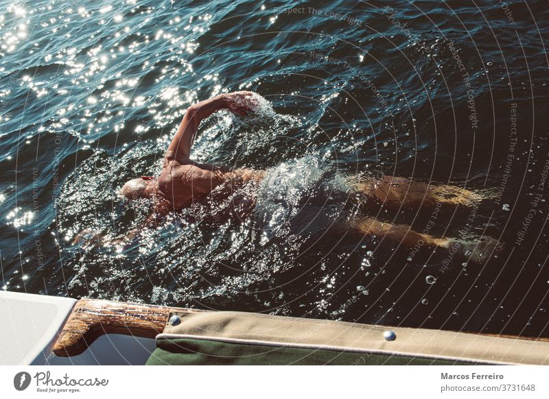 older man swimming in the sea next to his boat recreation calm outdoor european sailing activity exercise yacht tourism beautiful people vacation lifestyle