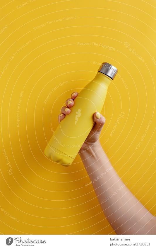 Close up of female hand, holding yellow reusable steel bottle on yellow background monochrome ecologic water thermo bright mockup woman faceless aluminum blank