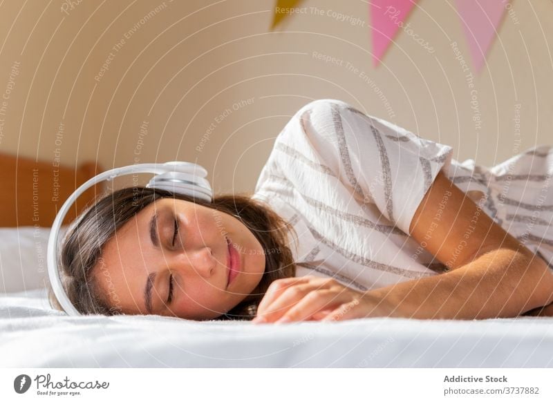 Young woman listening to music on bed headphones home cozy weekend eyes closed rest female lying gadget device bedroom young relax lifestyle sleep joy apartment