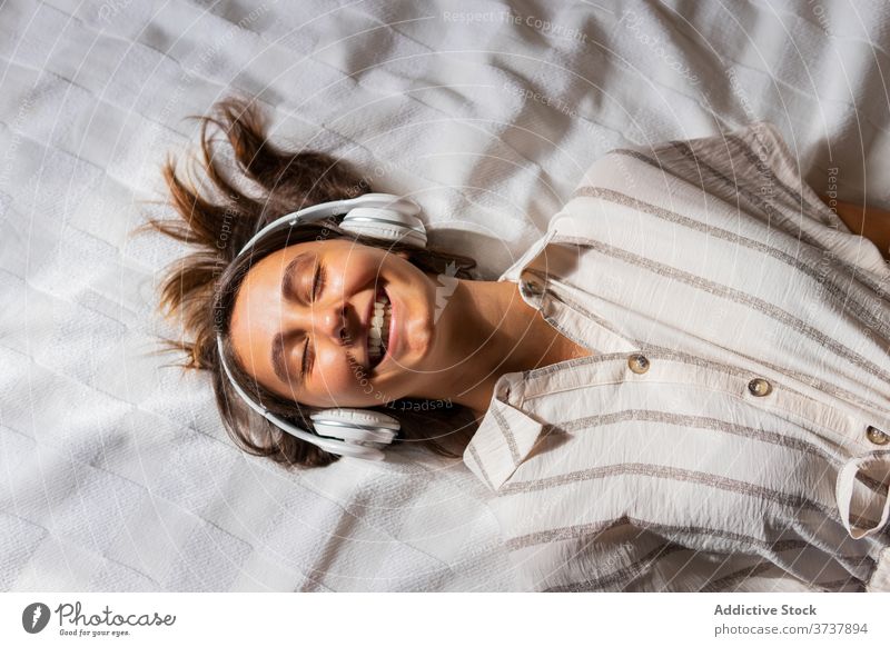 Content woman in headphones on bed music listen enjoy child together wireless entertain female lying gadget happy bedroom cheerful comfort smile home relax cozy
