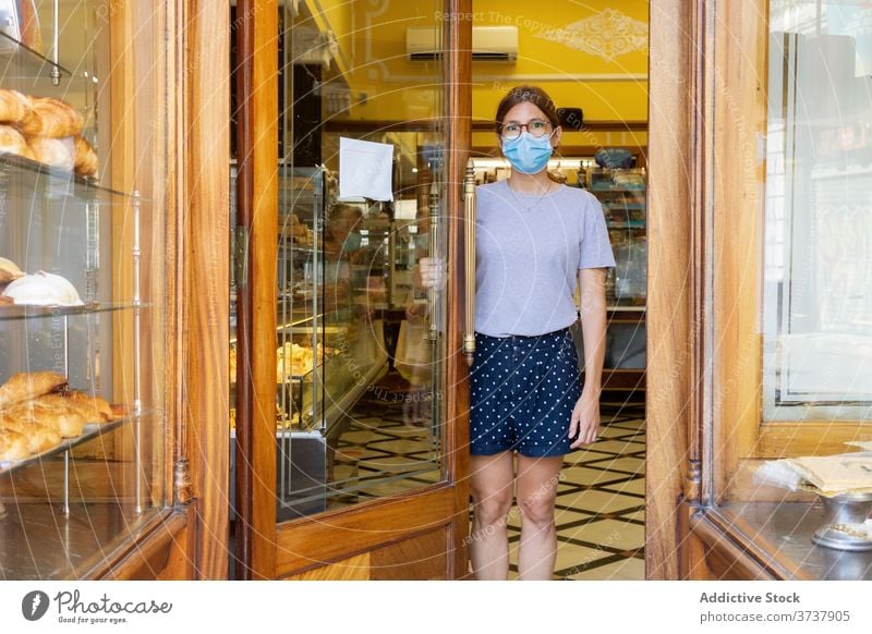 Woman in mask in bakery bakehouse seller woman interior door doorway medical covid female cozy stand new normal safety staff protect profession specialist