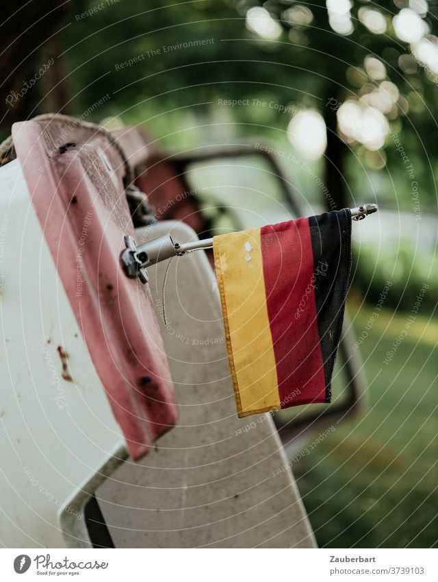 Small motorboat on land, leaning against a tree, with german flag Motorboat German flag country Stranded Old Decline tip tilted Plastic fuselage Ajar Futile