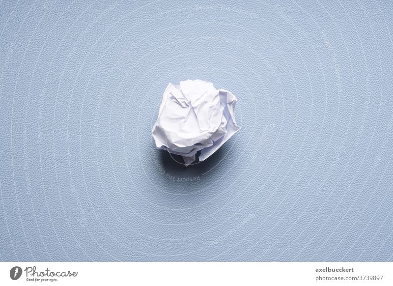 crumpled-up ball of paper on blue background balled discard dispose scrap throw away concept fail problem idea desk pad sheet trash rejection scrunch wastepaper