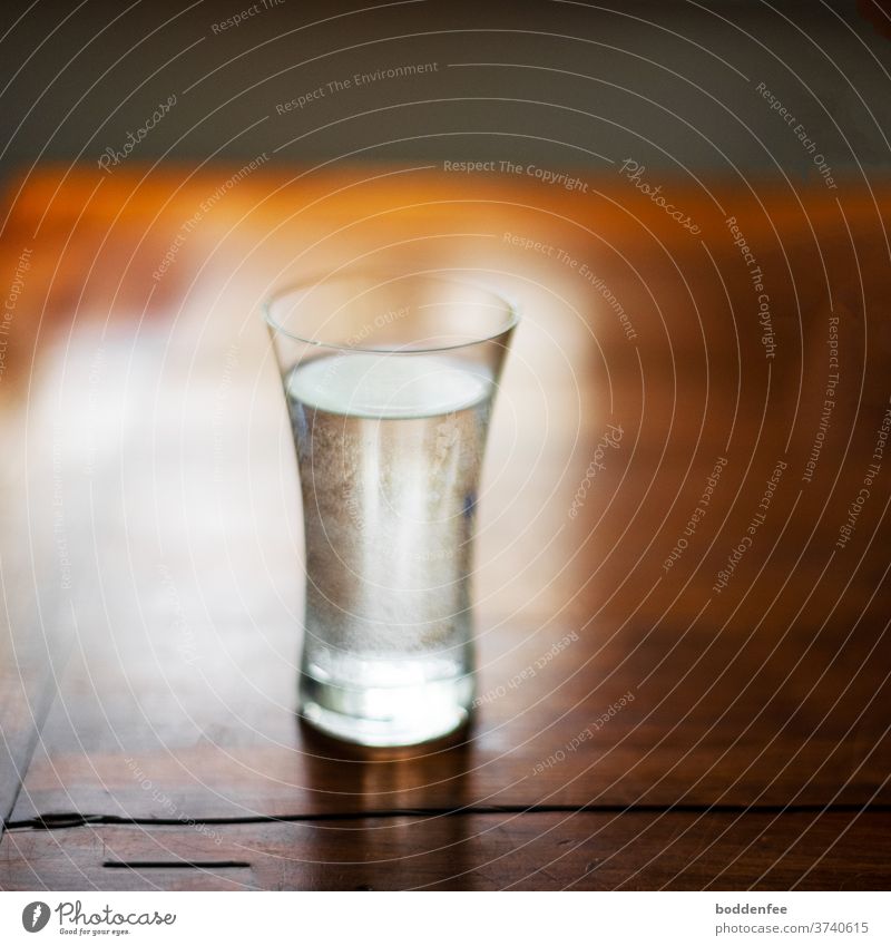 a water glass with co2-beads on the inside edge of the glass on an old, brown lacquered wooden table in the morning backlight, slightly blurred morning light