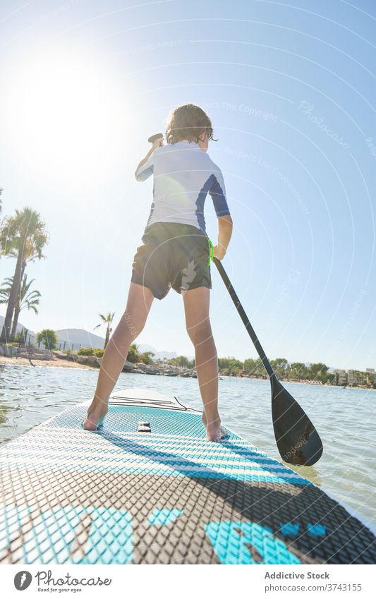 Vertical photo of a child in his back standing on a paddle surfboard rowing in the middle of the sea lifestyles surfing feet quiet fit recreation joy relaxation