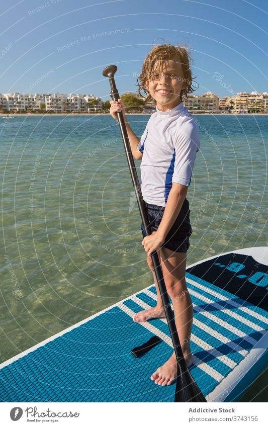 Portrait of a boy standing on a paddle surfboard with a paddle facing the camera lifestyles effort pose surfing trend feet quiet fit recreation joy relaxation