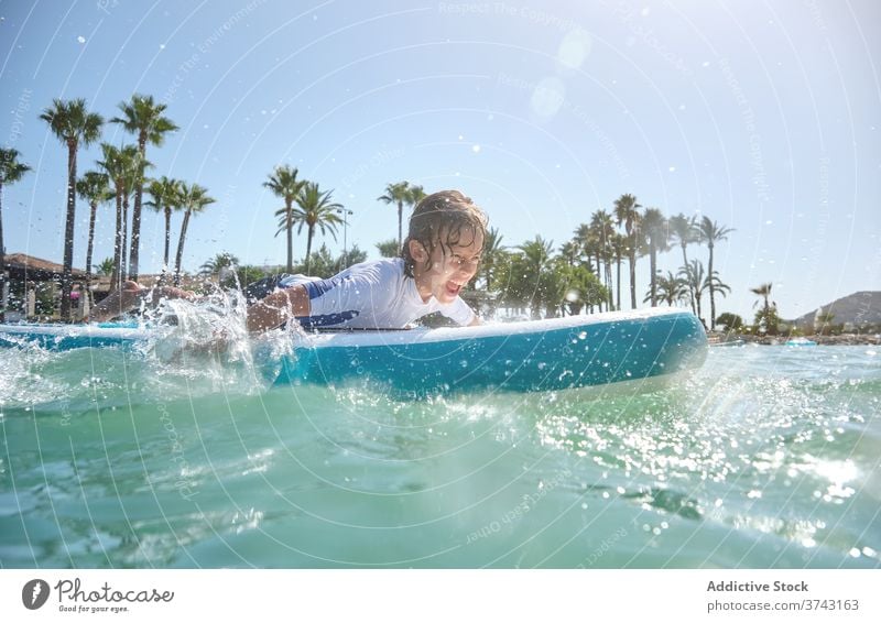 Boy lying on a surfboard paddling with his hands adolescence vitality excitement gesturing wellbeing splashing strength surfing teenage wavy concentration
