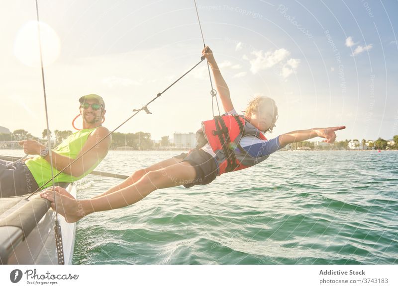 Boy attached to a rope from a boat hanging out to sea pointing to the horizon responsibility instructor racing teacher assistance gesture weight way wind