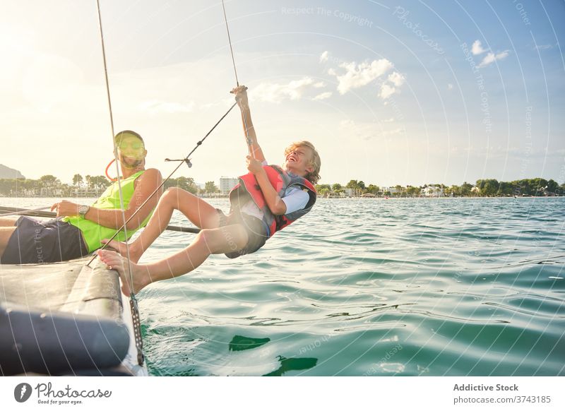 Boy with a life jacket laughing and grabbing a rope from a boat to make counterweights hanging out to sea gesture balance instructor racing teacher assistance