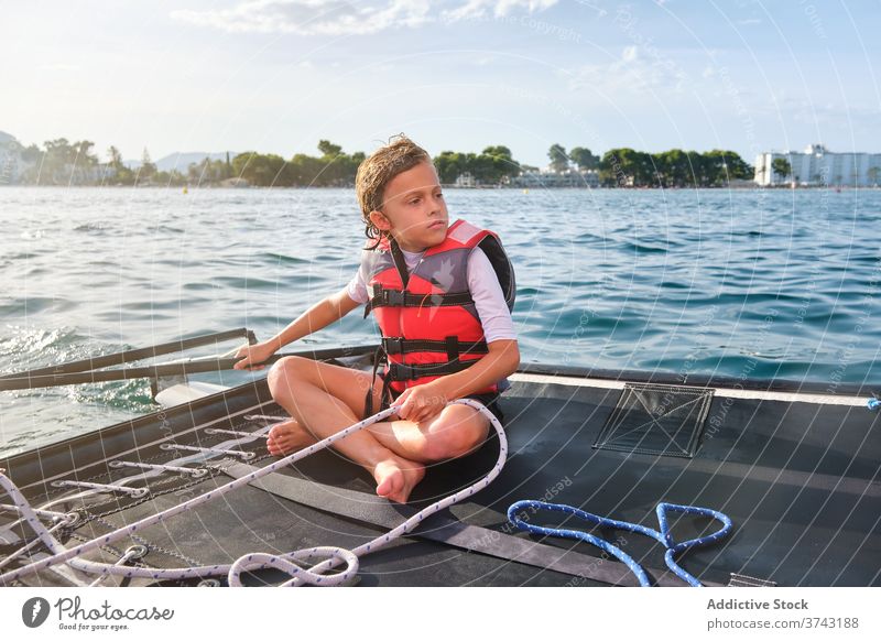 Serious kid in life jacket sitting in a boat holding the rudder serious child sailboat adventure sailing vacations seashore yacht yachting driving summer travel