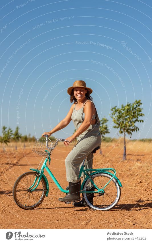 Calm woman on bicycle in rural area road sand sunlight overall bike countryside serene female sunglasses denim summer nature relax casual carefree vacation