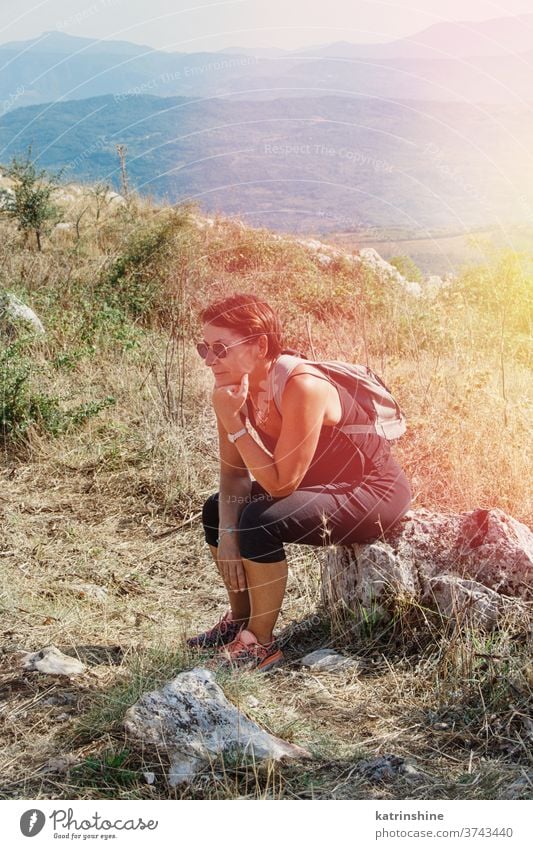 Female hiker takes a break in mountains in a sunny day Women hiking sit rest relax Sport nature outdoor acivity Recreation Trail Person Backpack Travel
