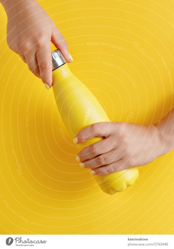 Close up of female hands, holding yellow reusable steel bottle on yellow background monochrome ecologic water thermo bright mockup woman faceless aluminum blank