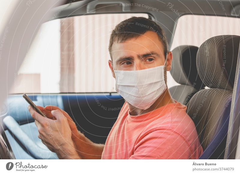 A young man, wearing a cloth face mask, checks the mobile phone inside the car people protective virus care adult person portrait protection beard t-shirt seat