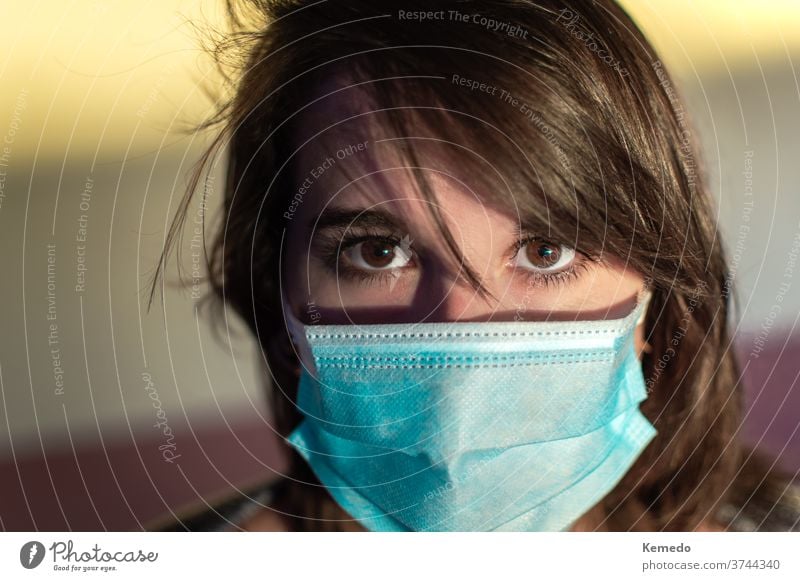Close up of young woman using surgical mask and looking at camera. person corona stare coronavirus portrait eyes face wearing sunshine sunny use millennial