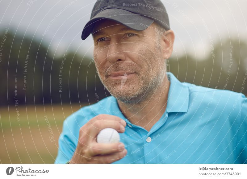 Middle-aged male golfer contemplating his shot staring down the fairway with a golf ball in his hand in a close up cropped portrait middle-aged man sports