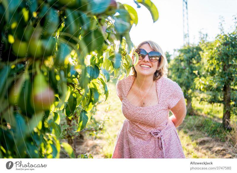 young blonde woman with sunglasses and pink dress laughing to camera in orchard Young woman Pink Dress Sunset Ease attentiveness closeness to nature pretty
