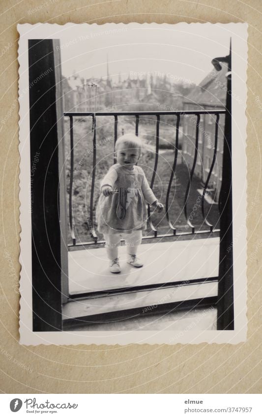 Memories of the 1960s - a black and white photo print with a deckle edge lies on beige paper and shows a little girl looking into the room from a balcony