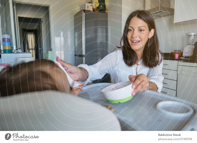 Woman feeding a baby sitting in a highchair sharing infant motherhood togetherness wellbeing bonding mouth toddler concentration skills furniture dining