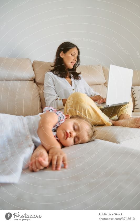 Toddler sleeping while her mother works with a laptop motherhood tenderness tranquility sofa responsibility newborn innocence toddler asleep peaceful wireless