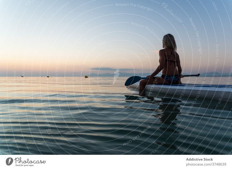 Anonymous woman practicing on paddleboard at sunset surfer sup board row sea training surfboard female summer sporty sit calm water sundown sky twilight dusk