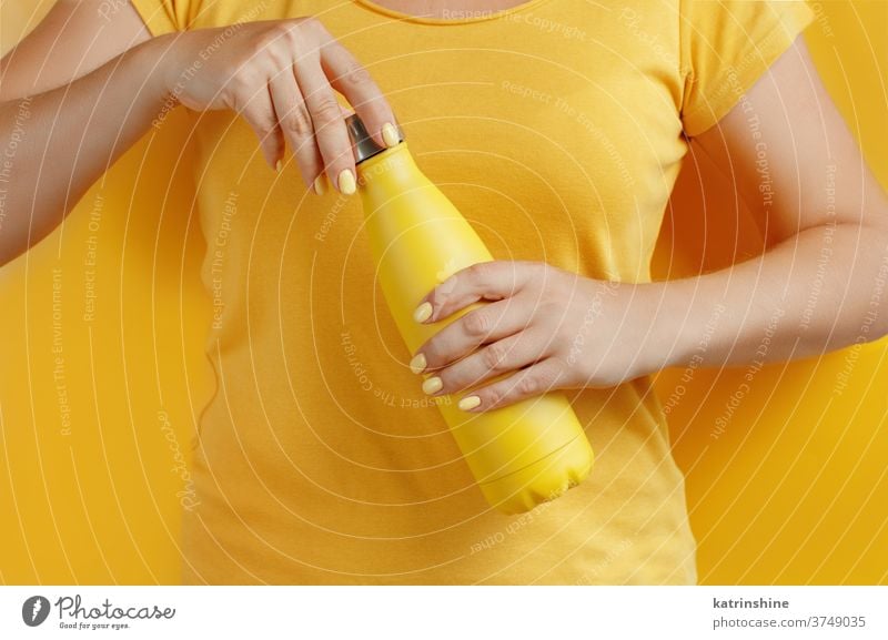 Close up of woman holding yellow reusable bottle on yellow background hand monochrome ecologic water steel thermo open bright mockup faceless aluminum blank
