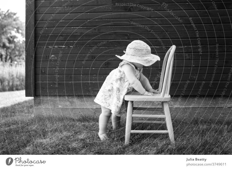 toddler wearing a sunhat holding onto chair to stand in front of a barn baby child 0 - 12 months childhood small cute relaxed candid cheeks quiet