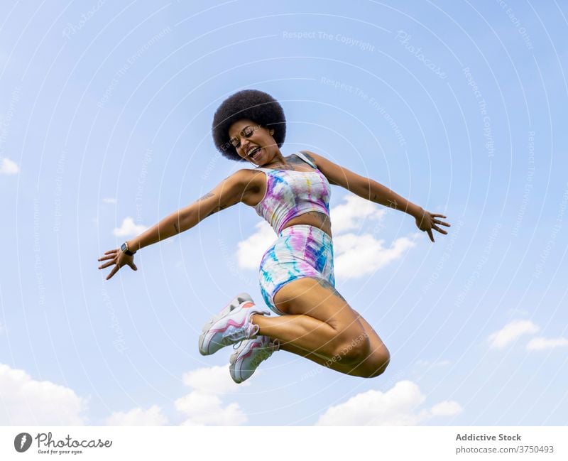 Cheerful black woman jumping against sky delight having fun moment excited cheerful outstretch summer female ethnic african american hairstyle afro outfit young