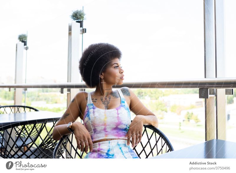 Tranquil ethnic woman on summer terrace of cafe wait order calm afro hairstyle city female black african american armchair sit chill relax rest thoughtful