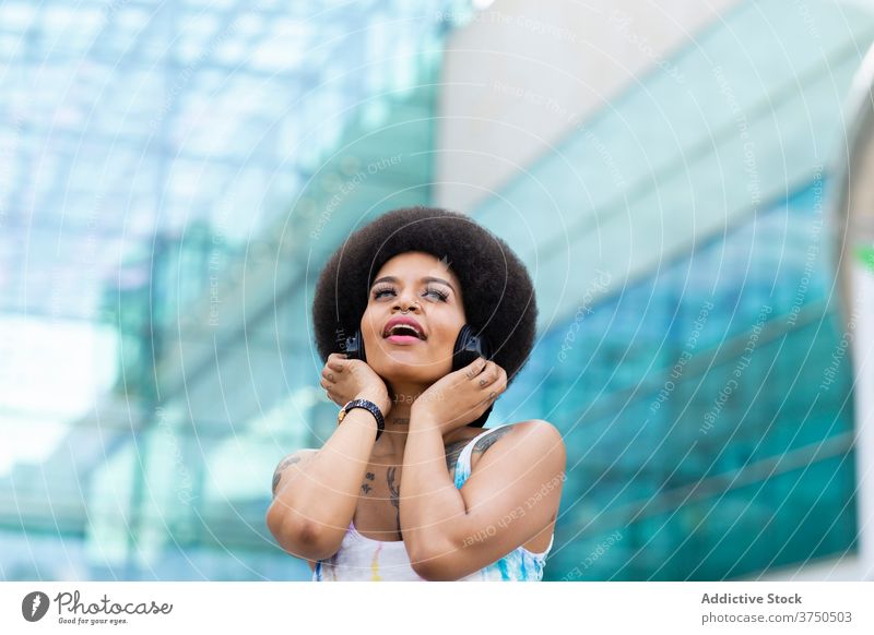 Dreamy black woman listening to music in headphones dreamy carefree enjoy song city urban ethnic african american afro hairstyle street device audio summer lady