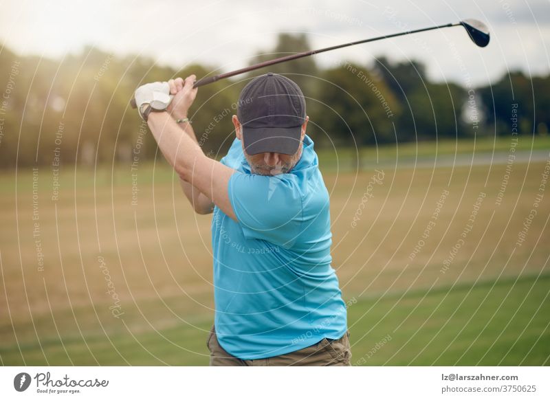 Man playing golf swinging at the ball as he plays his shot using a driver viewed from behind looking down the fairway in a healthy active lifestyle concept man