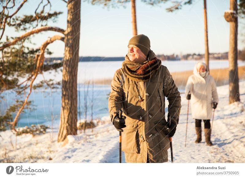 Winter sport in Finland - nordic walking. Man and Senior woman hiking in cold forest. Active people outdoors. Scenic peaceful Finnish landscape with snow.