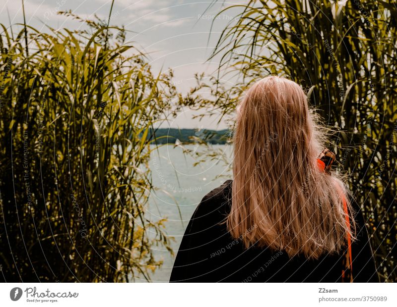 Young woman looks at the lake Lake Body of water Swimming lake bank Lakeside Sky Clouds Bushes bathe Relaxation relaxation vacation Bavaria Nature Exterior shot