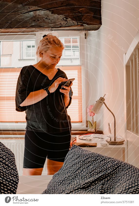 Young woman with smartphone in a hotel room communication mobile Communicate Room Bedroom Woman Blonde pretty relaxed fortunate smile Window Summer Sun Warmth