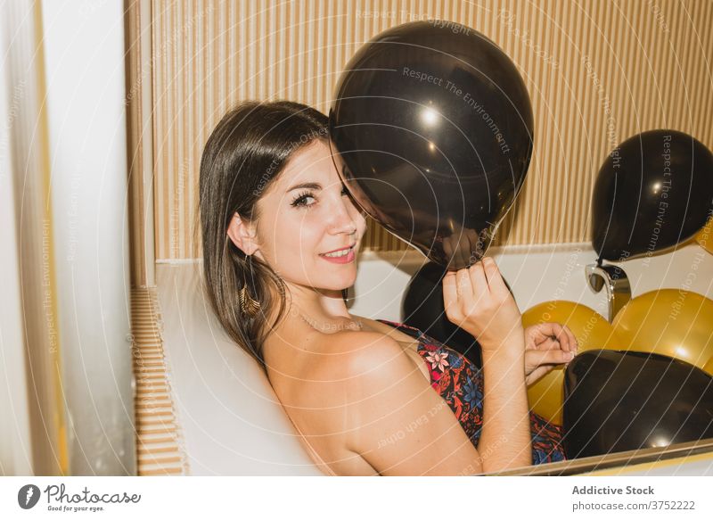 Young woman in bathtub with balloons after party tired festive celebrate holiday event laying down young female funny rest occasion xmas color new year relax